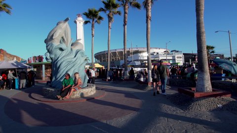 TIJUANA, MEXICO - NOVEMBER 28, 2021: Tourists walk near Playas de Tijuana (Spanish for "beaches of Tijuana"), the border between Mexico and USA. Statue with dolphins at the square