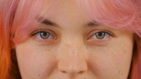 Video portrait of beautiful young woman with dyed pink hair looking in camera and away. Cute white girl with colored hair posing for video clip. Female with colored hair and green eyes looks in camera