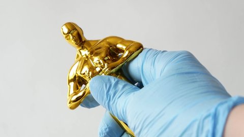 golden metal statue in hand with medical glove on white background. Hollywood Golden Oscar Academy award statue. Success and victory concept.