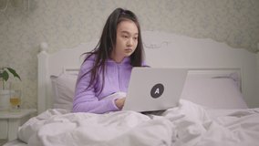 Tired Asian woman working from home using laptop sitting in bed. Angry female trowing away laptop in bed.