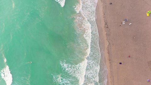 Vertical drone video over the waterline of a beach with crashing waves