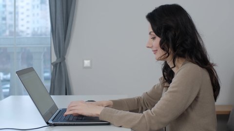 Freelancer woman working on laptop. Professioinal free lance writer typing text on notebook keyboard at home. Beautiful white female doing distant work on lockdown with cheerful smile in 4K video