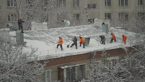 A lot of communal workers on the roof cleans snow