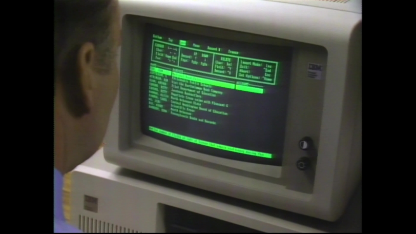 1980s Chicago, IL. Close Up of Man working on IBM PC Computer. Green Text or Source Code Background. 4K Scan from vintage broadcast VHS Betacam Master 