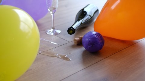 Messy Dirty Room with Empty Sparkling Wine Champagne Bottle Drinking Glasses and Deflated Balloons Left on the Floor After Party Night