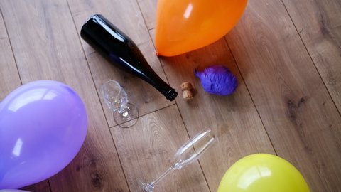 Messy Dirty Room with Empty Sparkling Wine Champagne Bottle Drinking Glasses and Deflated Balloons Left on the Floor After Party Night