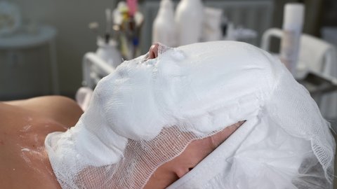 Woman with professional foam mask and gauze on her face in cosmetology clinic, side view. Making beauty procedure against facial wrinkles. Anti-aging effect.