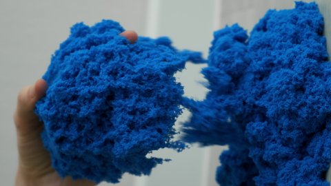 Sand is pouring from hands, vertical video. Close-up view woman's hands with kinetic sand of blue color. She plays with kinetic sand stirring it in her hands. Anti-stress toy for children and adults.