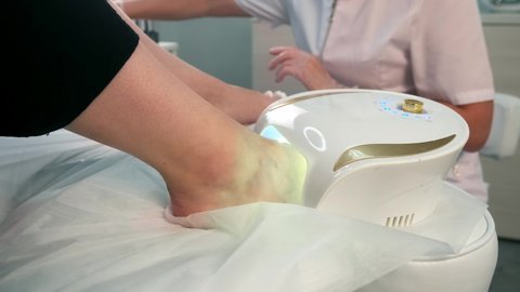 Woman is drying transparent base coal of shellac on nails on toes in UV lamp in beauty salon. Hygiene and care for feet. Professional pedicure in cosmetology clinic.