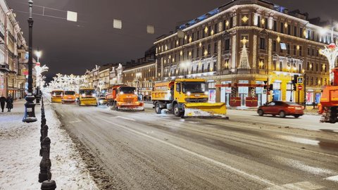 Russia, St. Petersburg, 01 January 2022: Several snowplows simultaneously clean the main street from it, bright festive decorations of the city for the New Year, work of public utilities