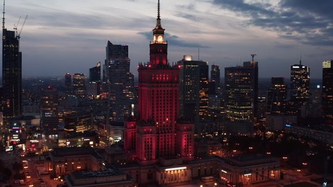 Evening slide and pan footage of red illuminated iconic Palace of Culture and Science. Downtown skyscrapers in background. Warsaw, Poland