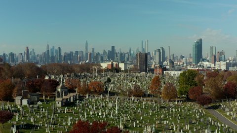 Forwards fly above historic Calvary Cemetery. Old tombstones on green lawn between autumn coloured trees. Skyline with Manhattan skyscrapers. Queens, New York City, USA