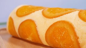 Motion video close up of orange cake roll with slice orange fruit on wooden plate.