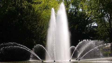 Germany, Dortmund, June 13st, 2021, 4:41 p.m., jets of water spurting out from nozzles  of a fountain in strong backlight in front of a green tree background. The water droplets sparkle in the sun