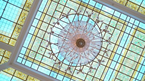 stained glass window. bottom-up view glass ceiling, multicolored transparent frames with patterns. interior element. large round chandelier with crystals and electric lamps. camera rotation