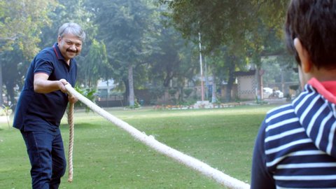 A senior man and his cute grandson enjoy playing a tug of war game together. An elderly man and his adorable grandchild doing a fun activity outdoors - leisure time, sports activity, family bonding