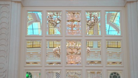 crystal chandeliers under tall stained glass window reflected in mirror. royal interior part. white marble walls and colored glass ceiling. meeting room luxurious expensive interior. king style hall