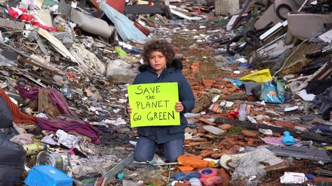7-year-old child environmentalist and ecologist holding a sign with the words save the planet go green, protest against climate change, global warming and atmospheric pollution in a garbage dump 