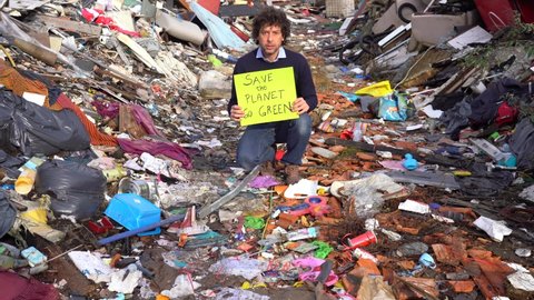 Man  40 years old ecologist holding a sign with the words save the planet go green, protest against climate change, global warming and atmospheric pollution in a garbage dump waste