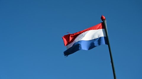 Waving flag of Netherlands on flagpole. Holland flag flying on the wind. Red, white and blue colors on Holland flag against blue sky. Dutch flag.