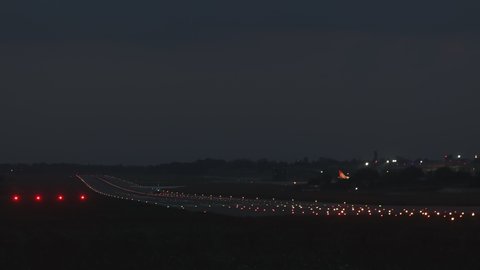 A passenger plane is making a landing on the runway. It's night outside and you can see the airport lights. 4K 50fps