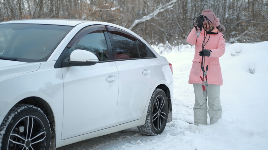 Confused Young Caucasian Woman Trying to Decide how to Use Starter Cables while Standing by the Car with Discharged Battery in Cold Winter Weather | Shutterstock HD Video #1084768189