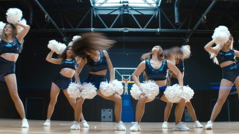 HANDHELD Female cheerleaders team performing a dance during a basketball game intermission