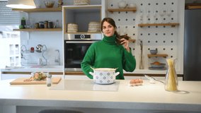 Young vlogger woman vlogging about cooking at her apartment domestic kitchen cook and making video vlog with smartphone as online content creator for internet. Female influencer making a meal.