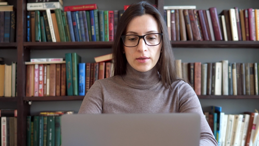College student uses a laptop to watch online distance learning, a seminar, a distance university webinar, or conduct a virtual classroom meeting in the university's creative space. The girl works on Royalty-Free Stock Footage #1084772113