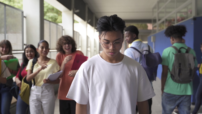 Sad Asian teenager victim of bullying at the High School. Abused Bullied student is hit by boy while group of classmates make fun of him. Violence and racism problem in Education | Shutterstock HD Video #1084772197