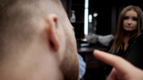 Brutal man in a barbershop looks at himself in the mirror and straightens his beard: Gomel, Belarus - July 2020