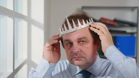 Portrait of smug man puts crown on his head with pride, megalomania.