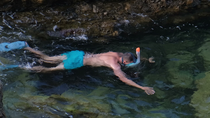 Enthusiastic diver swimming between rocks studying underwater inhabitants and the bottom