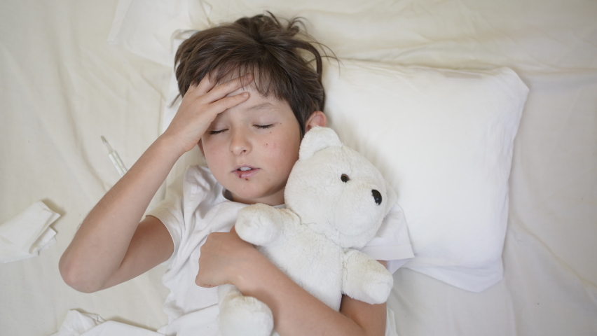 Sick child boy with fever lying on pillow in bed with teddy bear. Tired lack of energy preschool kid, temperature, fever flu symptoms and treatment, children medical healthcare, corona virus symptoms Royalty-Free Stock Footage #1084782103