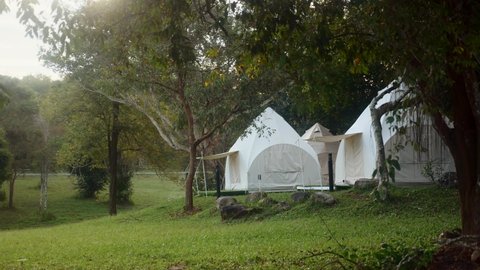 Morning in forest. Group of outdoor camping teepee tents, sunrise light in green lawn. Glamping campground on misty summer morning. Comfortable vacation trip in Khao Yai National Park in Thailand