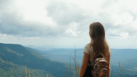 Inspiration adventure travel. Back view of woman with backpack standing on top of mountain, enjoy summer nature and touch her long hair by hand. Happiness, wanderlust and freedom concept. 4k