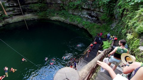 TIZIMIN, MEXICO - NOVEMBER 27, 2021: Tourists walk downstair and swim in the lake of Cenote La Xtabay, natural pit resulting from the collapse of limestone bedrock that exposes groundwater