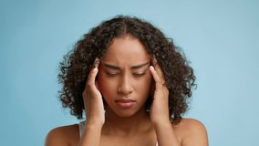 Headache. Unhappy African American Woman Suffering From Migraine Pain Massaging Temples Looking At Camera Standing Over Blue Studio Background. Health Problems Concept