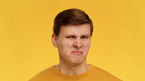 Disgusted Young Man Grimacing Smelling Bad Stink Posing Looking At Camera Expressing Negative Emotions Standing Over Yellow Background In Studio. Slow Motion