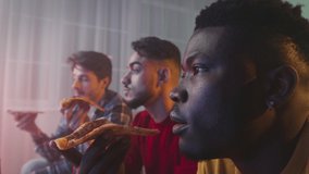 Male careless pastime. Three multiethnic guys friends eating delivered fresh pizza, watching tv together at home in evening, zoom out portrait, side view, slow motion - Powered by Shutterstock - Get 15% off with code: PIKWIZARD15