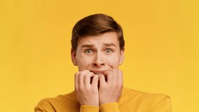 Anxiety And Fear. Scared Guy Biting Nails Looking At Camera Posing Standing Over Yellow Studio Background. Portrait Of Worried And Anxious Millennial Man. Slowmo