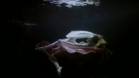 dreaming woman floating in dark depth of sea or ocean, magical dream, underwater slow motion shot