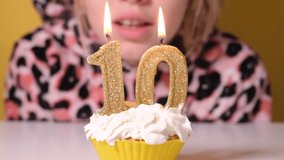 Happy teen girl in leopard Overalls blows out number 10 candle on birthday cake at party. Close up on girl face. Slow motion happy birthday video banner