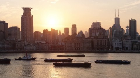 Shanghai, China - Dec.31, 2021: Time lapse footage of sunset in the Bund, historical landmark building skyline and Huangpu river, sun falling behind buildings with ships sailing on river, 4k video.