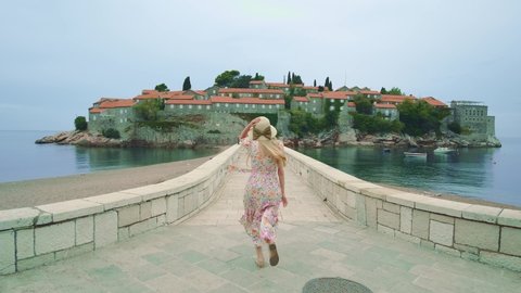 Woman running to the dream place laid on water. Long stone bridge leading to the island. Summer time. Sveti Sveti Stefan (Saint Stephen) island in the background.