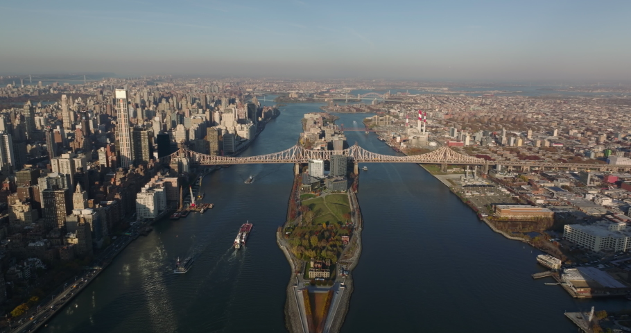 Aerial panoramic view of Roosevelt Island and long Queensboro Bridge. Cargo ships floating on East River in late afternoon. Manhattan, New York City, USA Royalty-Free Stock Footage #1084799257