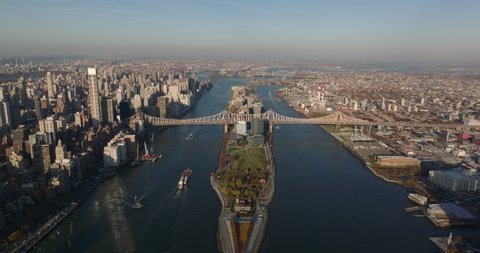 Aerial panoramic view of Roosevelt Island and long Queensboro Bridge. Cargo ships floating on East River in late afternoon. Manhattan, New York City, USA
