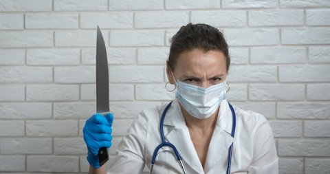 Doctor looking at knife. A doctor with dangerous look at a big knife in her hand.