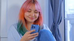 Happy young woman using mobile phone. Beautiful white girl with dyed hair browsing social media app on modern smartphone with cheerful smile. Individual female with rainbow colored hair filmed in 4K