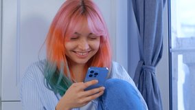 Happy young woman using mobile phone. Beautiful white girl with dyed hair browsing social media app on modern smartphone with cheerful smile. Individual female with rainbow colored hair filmed in 4K